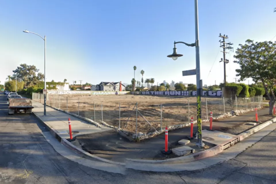 Google street view of vacant fenced-in dirt lot in South Los Angeles with graffiti on wall in background.